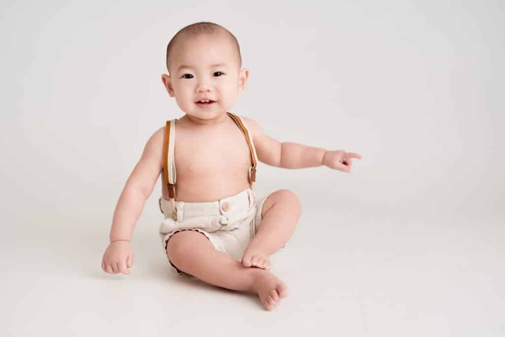 Cute asian baby boy smiling and wearing cute shorts with suspenders for a Sacramento Milestone Session.