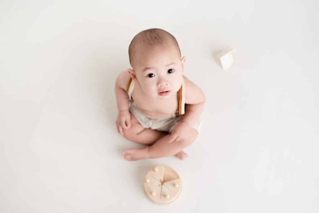 Baby boy playing with a wooden cake looking up during his Sacramento Baby Photography session.