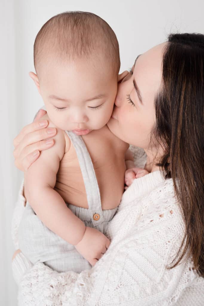 Asian mom kissing the cheek of her baby boy.