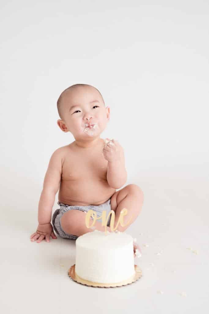 Baby smiling and eating cake during Sacramento Cake Smash in the Sweet Jean Photography Studio.