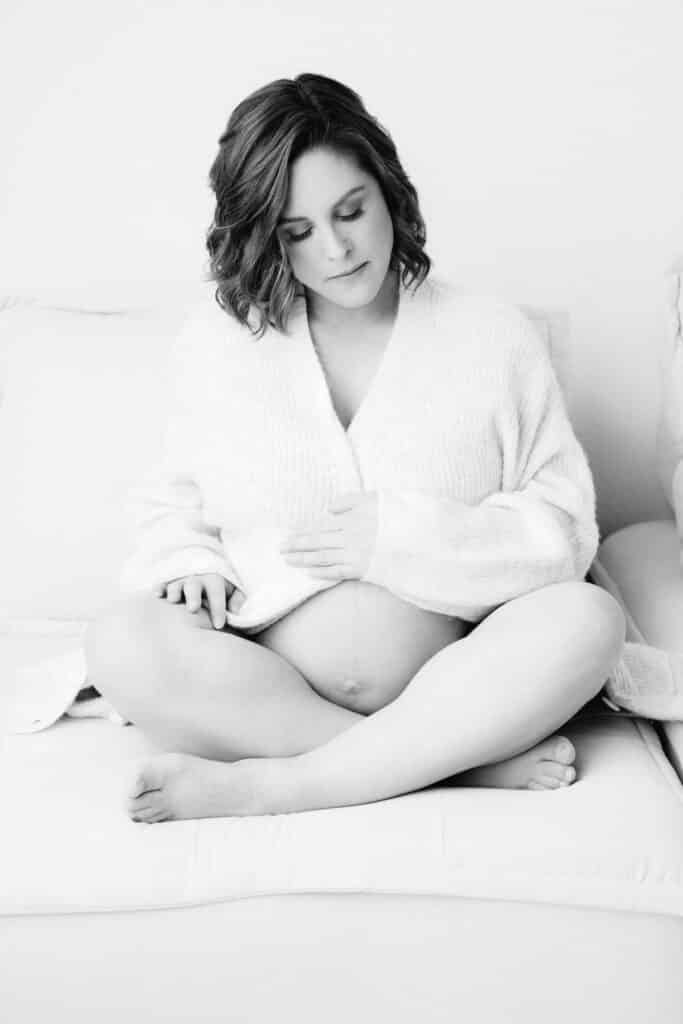 Pregnant woman in an oversized sweater gently holding her belly in black & white.